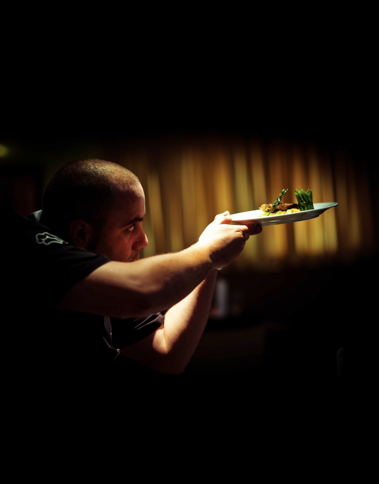 Chef presenting a plated fine-dining dish under dramatic golden light